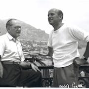 Black and white photograph of two older men looking off into the distance with a coast view behind them