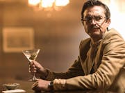 A white man sitting at a bar with a martini in hand looking perturbed