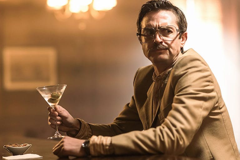 A white man sitting at a bar with a martini in hand looking perturbed