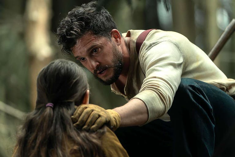 A young man looking seriously at a young girl with his hand on her shoulder protectively