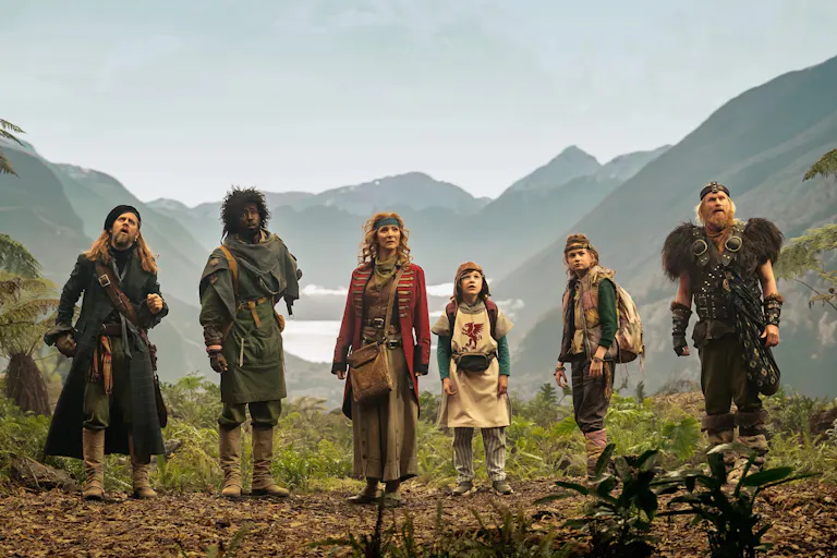 A group of adults and children wearing elaborate costumes, a vast mountainous scene in the background