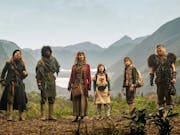 A group of adults and children wearing elaborate costumes, a vast mountainous scene in the background