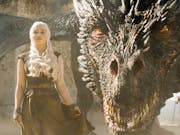 A young white man with bright white hair stands defiant as a huge, scaled dragon with amber eyes crouches behind