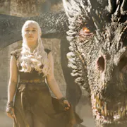 A young white man with bright white hair stands defiant as a huge, scaled dragon with amber eyes crouches behind
