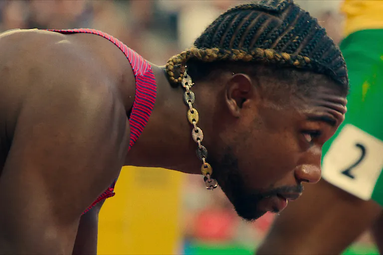 Close up of a strong young Black man with a decorative gold chain dangling around his neck as he crouches down in the starting blocks