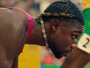 Close up of a strong young Black man with a decorative gold chain dangling around his neck as he crouches down in the starting blocks