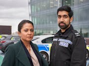 A Brown woman detective and a young brown policeman in uniform standing in front of a police car
