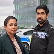 A Brown woman detective and a young brown policeman in uniform standing in front of a police car
