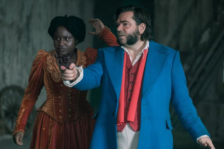 A Black woman in orange velvet corset dress and a white man with large mutton chops and wearing a blue jacket and red waistcoat, pointing at something