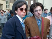 Two white teen boys in school uniforms and 80s clothing and hairstyles looking thoughtful