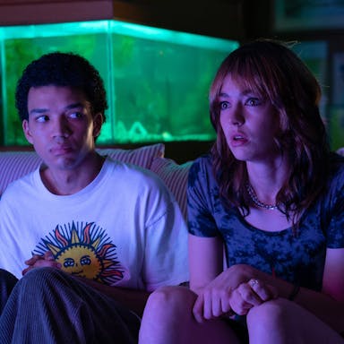 A young Black teenage boy and young white teenage girl look transfixed with a purple glow across their faces