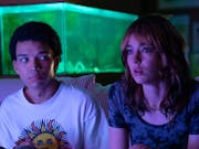 A young Black teenage boy and young white teenage girl look transfixed with a purple glow across their faces