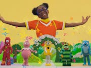 A young Black girl with hair puffs and glasses arms joyfully outstretched in a colourful fantasy land with five wacky monster characters in below