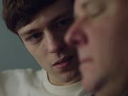 Close up of a young white man with brown hair looking at an older white man in the foreground