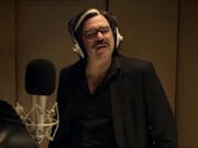 A white man with a grey streak in his hair in a recording booth