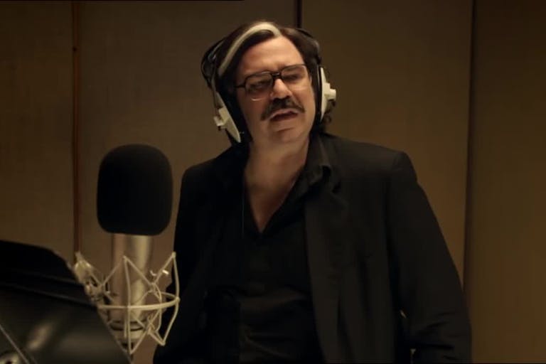 A white man with a grey streak in his hair in a recording booth
