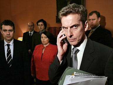 A group of white men in suits and one white woman in a red dress suit standing in a government office