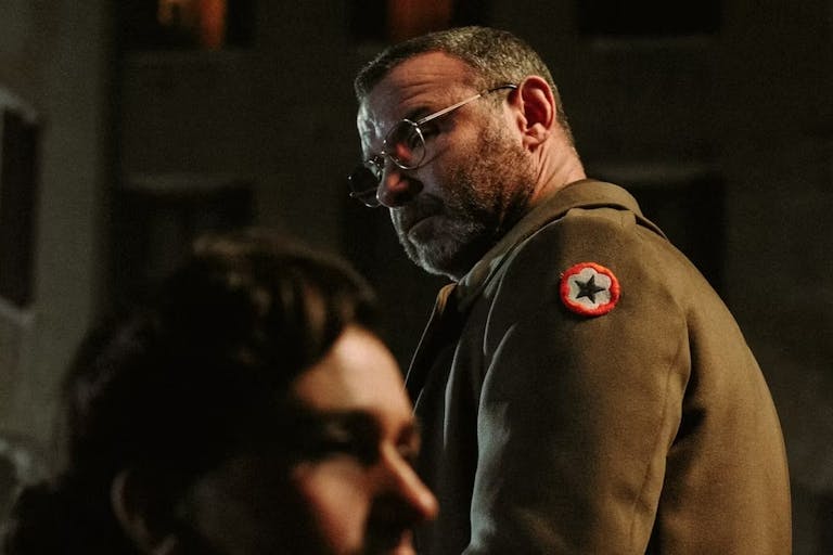 A white greying man in a WWII uniform looking over his shoulder with a white woman in the foreground