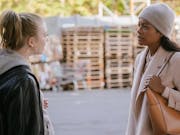 A white woman in a hoodie facing a Black woman in a smart coat, having a heated conversation