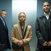 A young Black woman and man in suits stand in a lift with an older American Chinese man in the background
