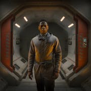 A young Black man in in brown overalls stands in a cinematic spaceship entrance looking shocked