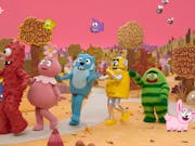Colourful robots and other creatures dance on a fantastically colourful set with a pink sky and yellow earth