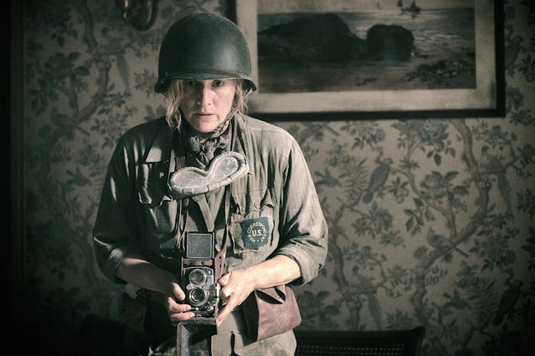 A white woman in army uniform holding a old style camera looking unnerved