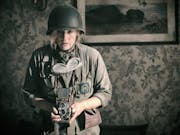 A white woman in army uniform holding a old style camera looking unnerved