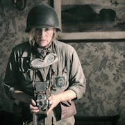 A white woman in army uniform holding a old style camera looking unnerved