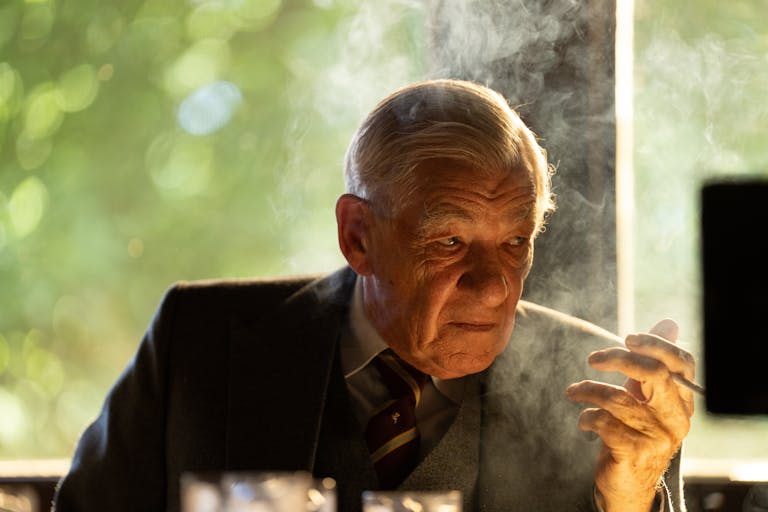 An old white man sitting at a desk smoking a cigarette looking menacing