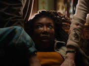 A black woman with long hair looking distressed as she is being grabbed by different hands
