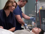 In a hopsital room, a patient is being checked by a white female doctor with long blonde hair. Another doctor is beside her checking an IV drip.