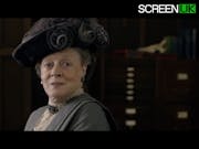 An old white woman in elegant period clothes and ornate hat looking happy and regal