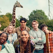 A varied group of teens smiling and posing in front of a giraffe