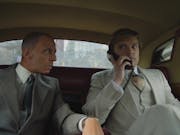 Two white men in expensive looking suits sitting in the back of a car