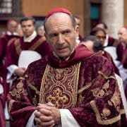 A middle aged white man in red velvet cardinal clothes surrounded by other men in similar clothing