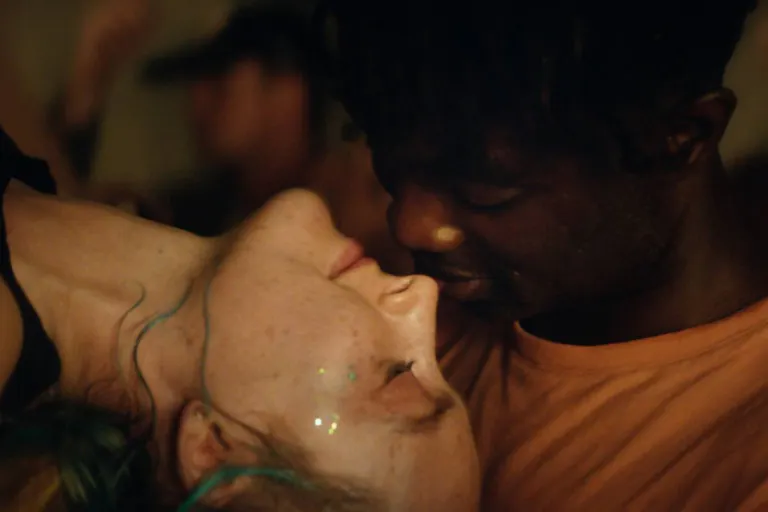 A young white woman with glitter on her face leaning back to kiss a young Black man