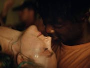 A young white woman with glitter on her face leaning back to kiss a young Black man
