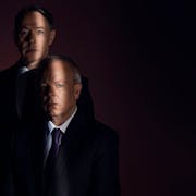 Two white men in suits staring straight ahead in the shadows with a single strip of light across their face