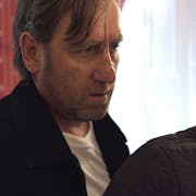 A white man looks menacingly over the shoulder of a worried looking white man