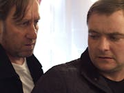 A white man looks menacingly over the shoulder of a worried looking white man
