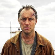 A white man with blood and scratches on his face standing on a dock looking troubled