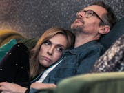 A white middle aged woman and man cuddling on the sofa with colourful scatter cushions looking forlorn