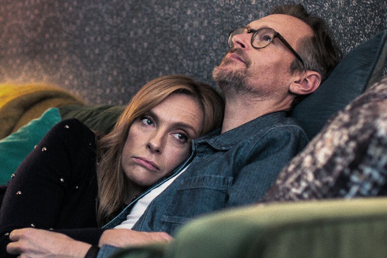 A white middle aged woman and man cuddling on the sofa with colourful scatter cushions looking forlorn