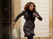 A white woman with short brown hair in dark clothing running out of a house with purpose