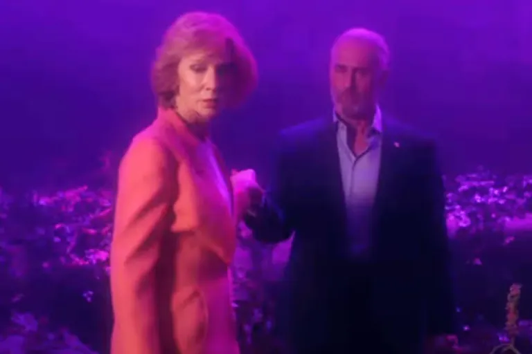 Dreamy purple and pink lighting over a white woman in a pink suit and a white man in a dark suit