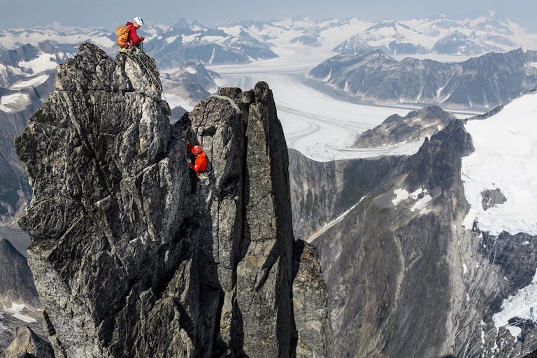 Aerial shot of an impressive, steep, snow topped mountain landscape with two climbers in red coats at the top