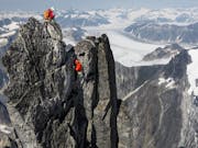 Aerial shot of an impressive, steep, snow topped mountain landscape with two climbers in red coats at the top