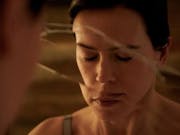 A white woman with cropped brown hair with closed eyes facing a fractured mirror