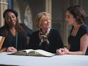 A middle aged Black woman, middle aged white woman and younger white woman in a church looking at a book curiously